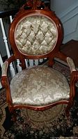 Frontal view of the antique accent parlor chair showing detailed wood carving on top and floral patterned upholstery on the front.