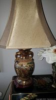 Full view of the oriental moriage ceramic lamp with beige fabric shade on a table.