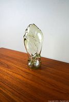 Front view of the art glass sculpture showing translucent greenish glass with internal yellow swirls, on wooden surface