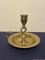 Brass chamberstick candle holder with twisted stem, round base, and handle shown from the side against plain background.
