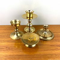 Four brass candle holders on wooden surface, showing different heights and base designs.