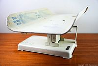 Angled top view of the vintage baby scale featuring the white curved metal tray with printed blue weight conversion charts and baby position outlines.