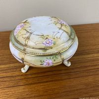 Oblique front side view of the circular footed trinket dish showing hand painted floral decoration and three feet.