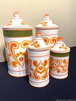 Four vintage ceramic kitchen canisters with bright orange paisley pattern, two with green stripes, arranged on dark surface