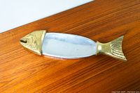 Top-down photo of vintage fish-shaped platter showing silver center and brass fish head and tail on wood surface.