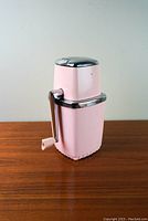 Front view of the pink ice crusher with metal and chrome handle and top lid.