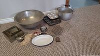 Overall shot of all kitchen bakeware, pans, muffin tins, measuring cups, cooling racks, enamel plate and antique lock arranged on carpet.