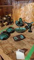 View of all seven pieces on plywood surface showing wall sconces, ashtrays, and figurines.