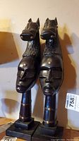 Pair of tall dark wooden bookends with carved horse heads and human faces, shown from front.