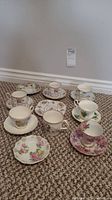 Top view showing nine different floral cups and saucers placed on carpet with various delicate patterns.