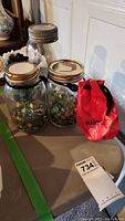 Three glass mason jars filled with colorful marbles and a red marble bag on a table.