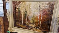 Front view of original signed forest scene painting in ornate white and gold frame.