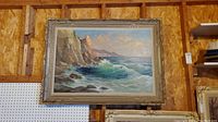Frontal view of the signed canvas painting depicting a coastal scene with cliffs and crashing waves, displayed on a wall.
