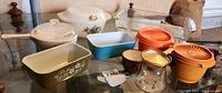 Assorted vintage kitchenware including Pyrex fridgies, Corning Ware pot, Arcopal bakeware, orange Tupperware containers, and small bowls