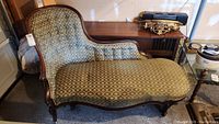 Front view of antique upholstered settee with green patterned fabric and carved wooden frame.