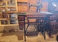Full view of Singer sewing machine mounted in wooden cabinet with treadle pedal and drawers.