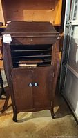 Full view of the Victrola grainophone cabinet showing its shape, wood finish, and front doors with blue knobs.