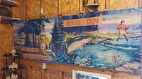 Full view of vintage Molson Export cardboard advertising sign hung on wooden wall, showing entire fishing scene with beer bottle and fisherman.