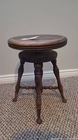 Full view of the vintage wooden piano stool showing the round seat, central adjustable mechanism, and carved wooden legs.