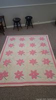 Full view of vintage quilt laid on floor showing rows of pink flower appliques and pink border.