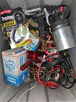 Photo showing assorted automotive accessories including Prestone tester, motor mounts, red signal light lens, wiring with connectors and clamps, pneumatic detail sander, and miscellaneous metal pieces.