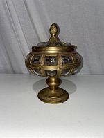 Full side view of the brass and glass potpourri canister on white surface with neutral background.