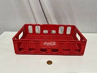 Red Coca Cola plastic soda crate with coin in front for scale and display.