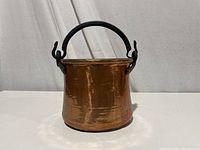 Image showing the copper pail from one side with visible hammered texture and black iron handle.