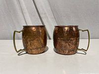 Two solid copper mugs with hammered texture, brass handles visible.