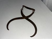Single ice block tongue with two curved rusty metal arms and wooden handle on white surface.