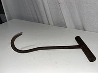 Metal ice hook placed diagonally on a white surface showing the curved hook and T-shaped handle.