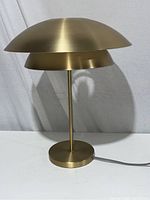 Brass colored dome shaped table lamp on white surface with gray background, showing the lamp turned off.