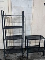 Full view of the taller four-shelf black wire storage unit next to the shorter two-shelf unit, both empty and against a wall.