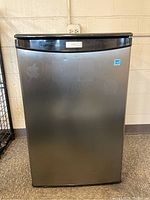 Front view of the mini refrigerator with stainless steel door showing smudges and wear.