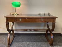 Full front view of wood desk showing curved legs, leather top, drawer, and green desk lamp