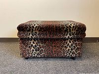 Front view of square ottoman covered in cheetah print fabric showing pattern and cushioned top.