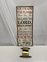 Photo showing vertical rectangular steel wall sign with Bible verse and small brass scroll with The Lord's Prayer.