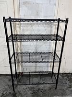 Front view of black metal wire storage shelf with four tiers, showing open design and metal wire shelves.