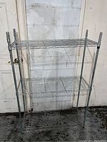 Front view of silver metal utility storage shelf showing three wire grid shelves and four vertical posts.