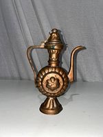 Full view of copper-colored Turkish style tea or coffee pot with a curved handle and long spout, floral embossed circular design on the body, standing on a flared base.