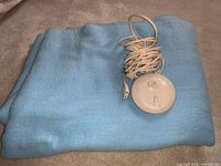 Folded baby blue electric blanket with white oval-shaped control unit and coiled cord