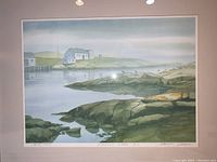Framed limited edition print showing a coastal scene with rocks, water, and buildings in distance. Pencil signature and numbering visible below image.