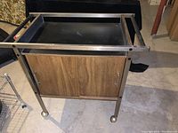 Full view of MCM bar cart showing wood-look sliding door cupboard, chrome frame, and wheels.
