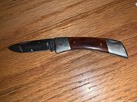 Opened folding pocket knife with visible wooden handle and metal bolsters, showing blade extended.