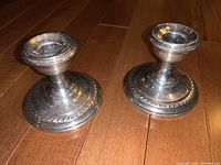 Pair of sterling weighted candlesticks placed on wooden floor, showing shape and details