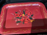 Small red metal Toleware tray featuring hand-painted red roses with green leaves and gold decorative swirls around the edges