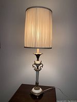 Full view of the Victorian style table lamp lit, showing the tall pleated fabric shade and ornate base