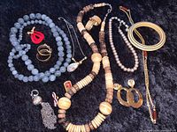 Photo of vintage costume jewelry assortment on black velvet, showing multiple necklaces, bracelets, and earrings in various colors and styles.