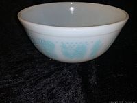 Side view of the Pyrex Amish Butterprint mixing bowl showing the turquoise farm-themed pattern on white milk glass.