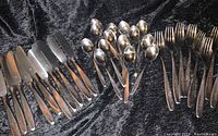All pieces spread out on black fabric showing knives, forks, and spoons in vintage WMF design.